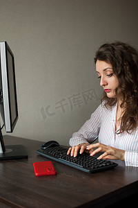 身着白衬衫和卷发的年轻女办公室经理坐在桌旁，用键盘打字，日常工作，自由职业者