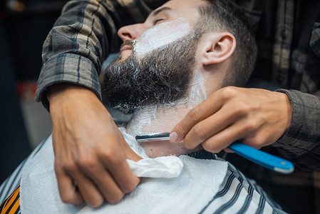 留着胡子的年轻男子在理发店被理发师刮胡子