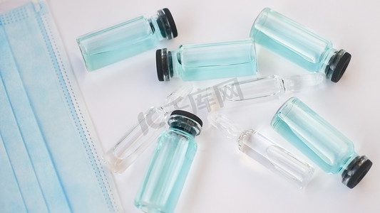 安瓿摄影照片_小瓶疫苗、白色背景上透明蓝色液体的玻璃安瓿顶视图、全球疫苗接种概念