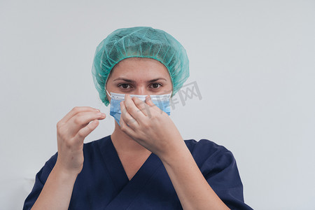 手术帽摄影照片_灰色背景下戴着医用口罩和手术帽的女医生或科学家的特写。