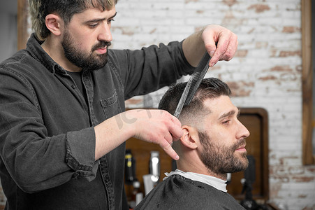 理发师用剪刀给一个英俊的年轻人剪头发。