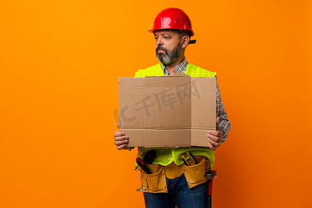 橙色背景下空海报的中年建筑工人