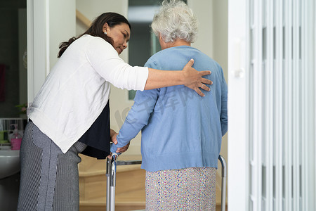 护理人员帮助亚洲或老年妇女在助行器支撑下走上家中的楼梯。
