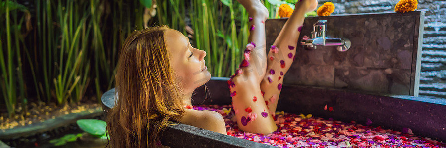 有魅力的年轻女子在沐浴着热带花卉和芳香油的花瓣。