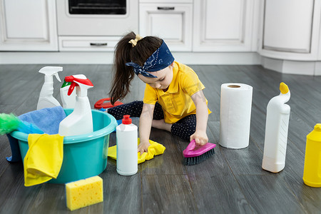 厨房刷子摄影照片_小女孩在清洁时在厨房地板上玩清洁剂和刷子