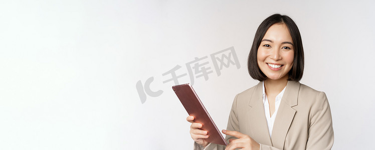 亚洲女商人、女售货员拿着数字平板电脑、微笑着、使用小工具、穿着西装站在白色背景上的形象