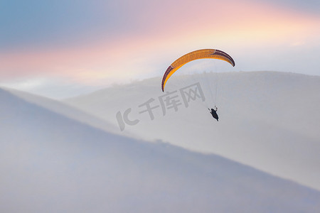 商务风宣传单摄影照片_滑翔伞正在丘陵地区的天空中计划