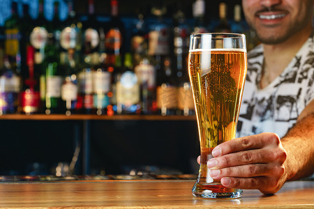 冰镇啤酒摄影照片_酒保在酒吧的吧台提供一杯冰镇啤酒