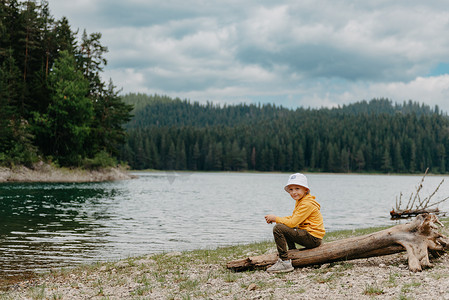 观山湖摄影照片_小男孩坐在山湖附近的圆木上。