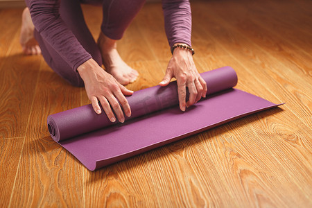 在家里的木地板上进行锻炼之前，一位女士的手铺着淡紫色的瑜伽垫或健身垫。