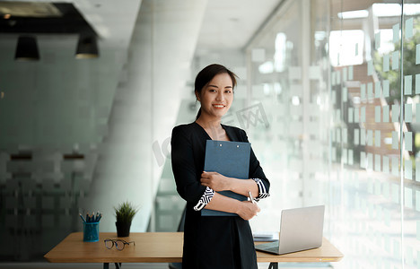 使用笔记本电脑和计算器进行财务会计工作时，自信的亚洲女商人站立着