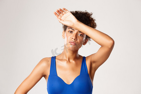 身着运动服、疲惫的年轻女运动员的特写镜头，在锻炼训练后擦去额头的汗水，站在白色背景下