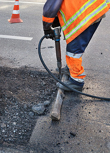 道路工人在修路时用手提钻清理一些沥青。
