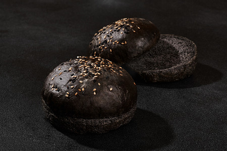 新鲜、烘烤、整体切成半黑或巧克力面包，在黑色背景下撒上芝麻，并有复制空间。