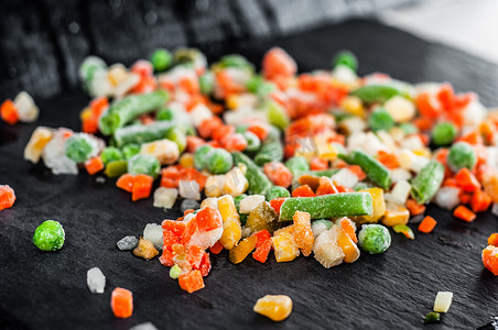 胡萝卜地摄影照片_石架上摆着不同鲜艳颜色的冷冻蔬菜的混合物