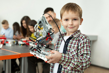 学校机器人课上一个聪明男孩的肖像，他手里拿着一个由计算机编程的塑料部件组装而成的机器人