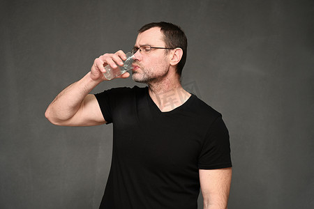 穿着黑色T恤和眼镜的中年男子从玻璃杯里喝水