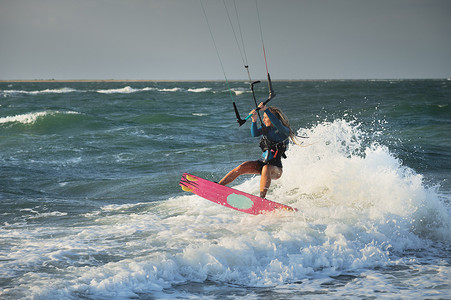 大海乘风破浪摄影照片_职业风筝冲浪白人女子在大风天气中乘风破浪。