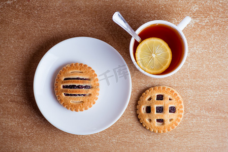 一杯茶和柠檬，桌面上碟子里放着果酱的饼干