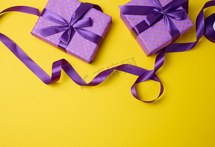 紫色礼品盒子摄影照片_用礼品紫色纸和丝带包装的盒子在黄色背景上，顶视图。
