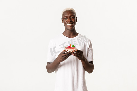 英俊快乐的非洲裔金发帅哥的肖像，庆祝生日，微笑着许愿，拿着生日蛋糕，站在白色背景