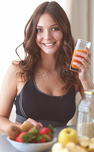 女孩坐在厨房里的桌子上，手里拿着水果和果汁杯