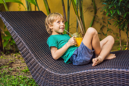男孩在玻璃梅森罐子里喝着多汁的芒果冰沙，水池背景上有钢吸管。