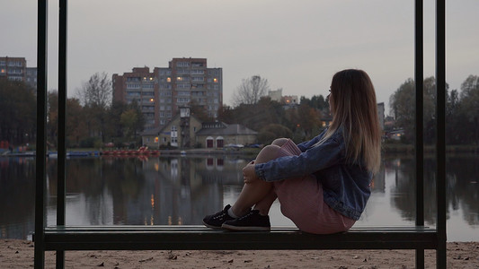 秋天的夜晚，一个孤独的年轻女孩坐在城市的长凳上。