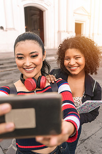 尼加拉瓜莱昂公共广场上两名多种族拉丁裔学生在户外用手机微笑自拍的垂直照片。