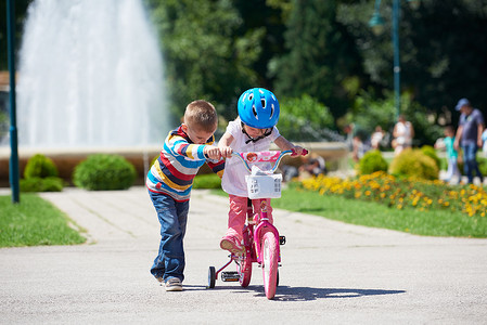 在公园学习摄影照片_男孩和女孩在公园学习骑自行车