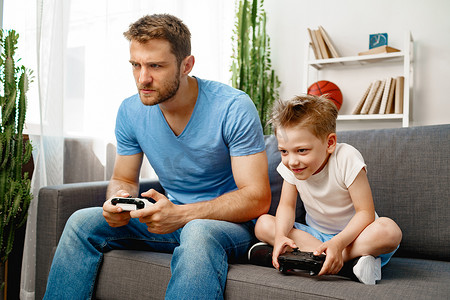 孩子电子游戏摄影照片_父亲和他的小儿子在家一起玩电子游戏