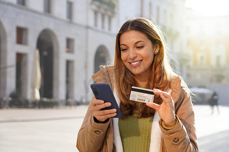 年轻女性在智能手机上输入信用卡号码的特写，可在网上购物或在户外检查银行账户