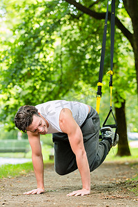 城市公园里的男人做悬挂训练器运动