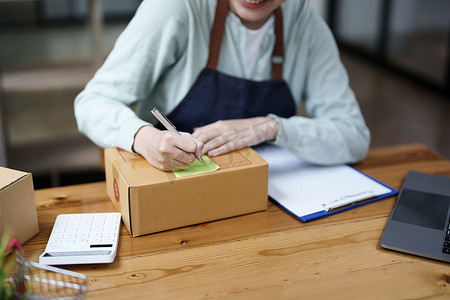 一家小型初创公司和中小企业主（一位亚洲女性企业家）的肖像，正在记事本上写下信息以整理产品，然后将其装入内盒中供客户使用