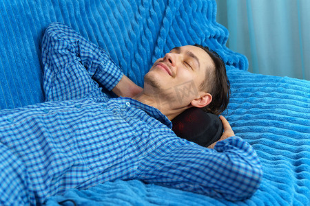男子躺在沙发上，用电动按摩枕按摩颈部。