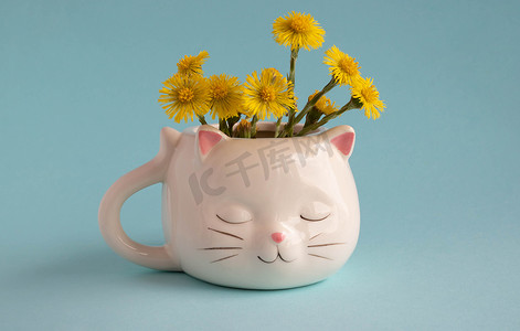 白色咖啡杯，形状像一只粉红色耳朵的猫，母亲和继母的花朵，蓝色背景的特写