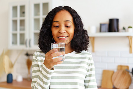 微笑的非洲裔美国女性站在厨房里享用一杯清水