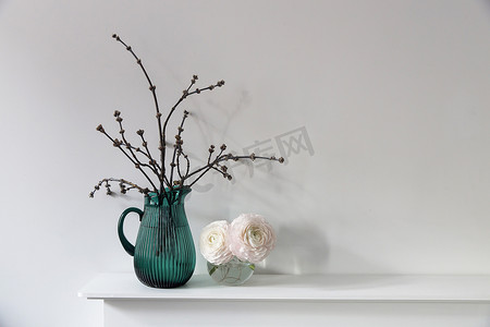 白色桌子上透明圆形花瓶中的三个淡粉色毛茛属植物。