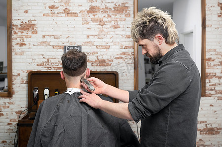 男理发师在理发店用剪刀给男性顾客剪头发。