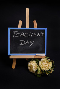 粉笔黑板的特写，上面写着教师节，站在木桌画架上，旁边是黑色闹钟，隔离在黑色背景上，有复制空间。