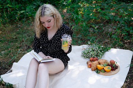 在公园里用格子布野餐的年轻女子的肖像，她正在读一本有美味小吃的书