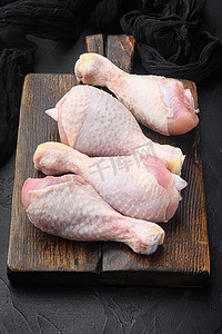 生鸡腿的原始切割，带有鸡大腿和鸡腿，在木切板上，在黑石背景上