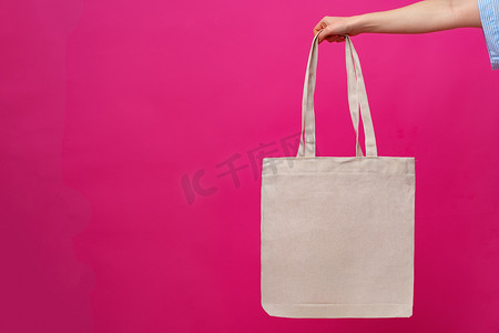 粉色背景下女手拿着生态或可重复使用的购物袋