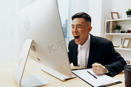 穿着西装、喝着咖啡的男人坐在电脑前的桌子旁
