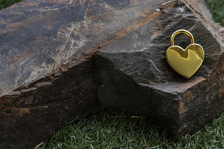 巨大心形背景摄影照片_在巨大的石头的金黄心形的爱挂锁在草背景。