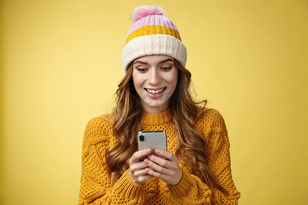 惊讶可爱的女孩收到好消息阅读令人兴奋的消息持有智能手机睁大眼睛微笑手机显示屏，玩很棒的手机游戏发短信，发送图片寒假