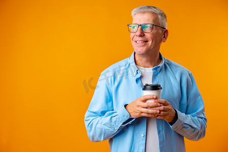 一杯咖啡摄影照片_黄色背景中戴眼镜的帅气老人拿着一杯咖啡