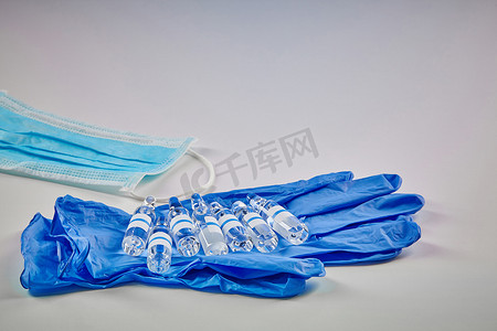 七个样机安瓿，蓝色一次性手套上装有透明液体，医用面罩上白色隔离。