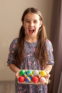 一个穿着裙子的有趣的黑发小女孩拿着一个装有彩蛋的纸板托盘