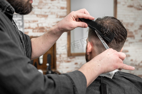 理发师用剪刀给一个英俊的年轻人剪头发。